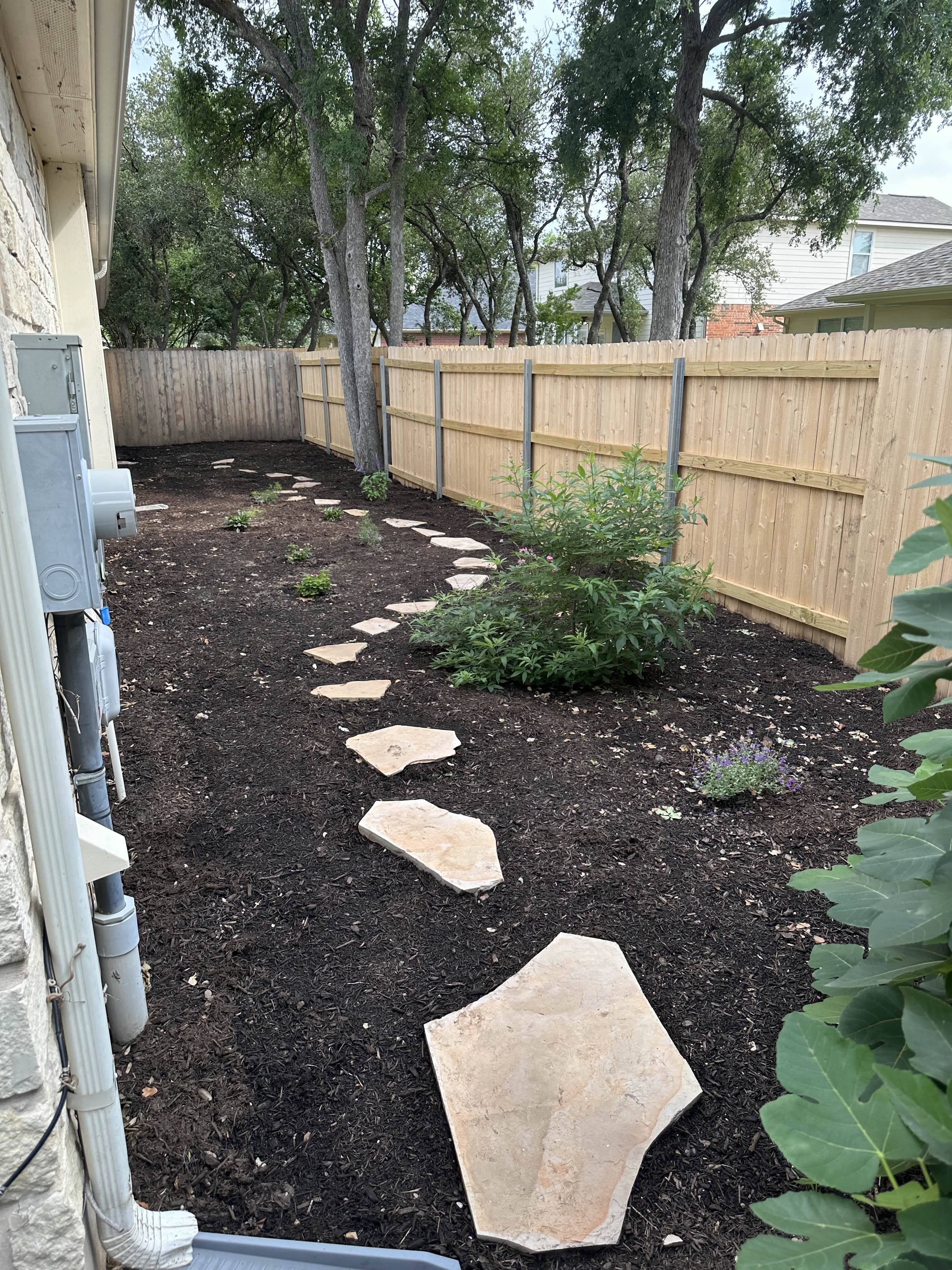 After - What was once a bare, unused side yard is now a clean, inviting garden path — complete with fresh brown mulch, native plants, and natural stone stepping stones for a polished, functional upgrade.